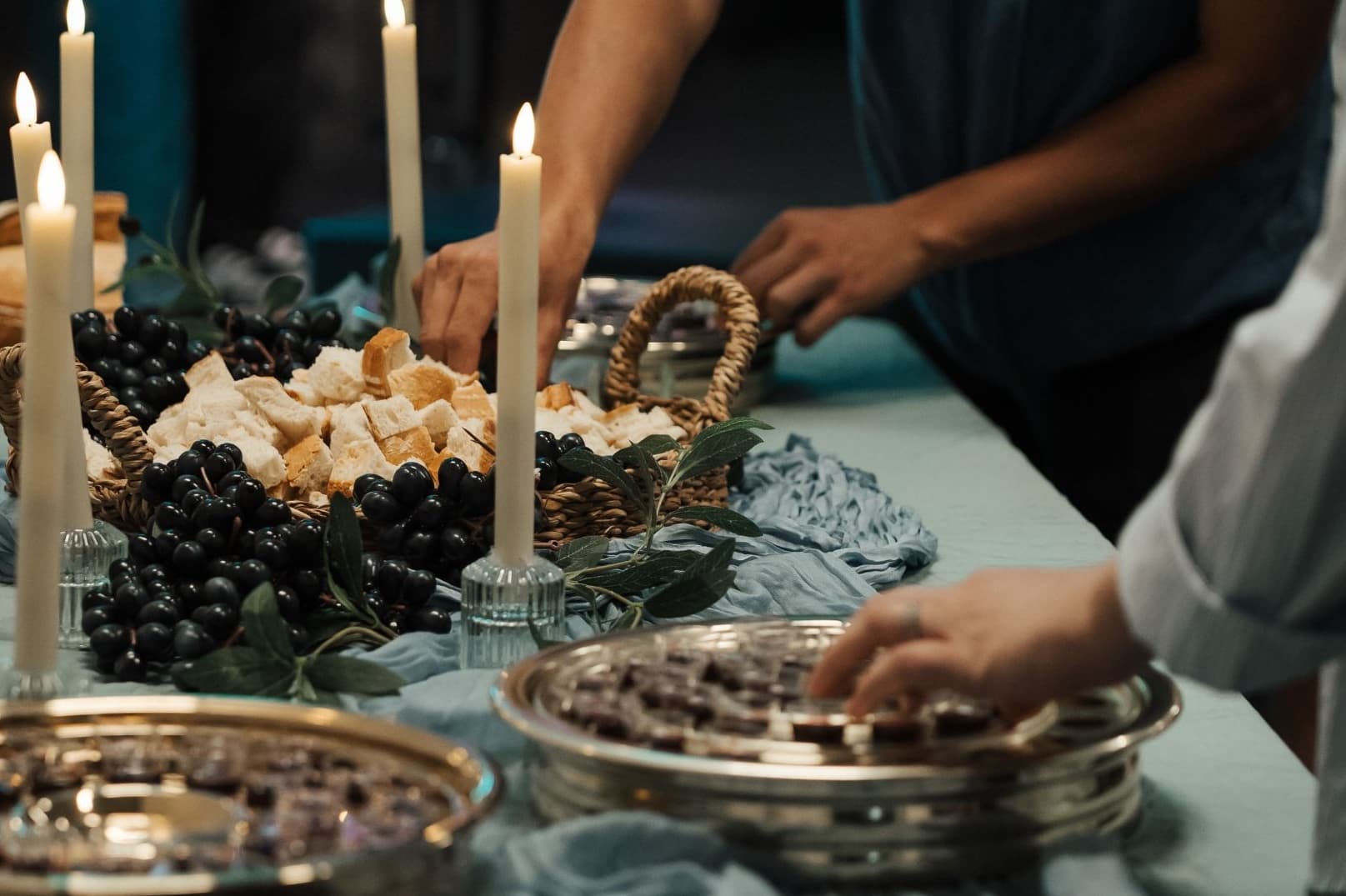 Communion laid out on table with candles and people's hands reaching to take bread and grape juice from the baskets