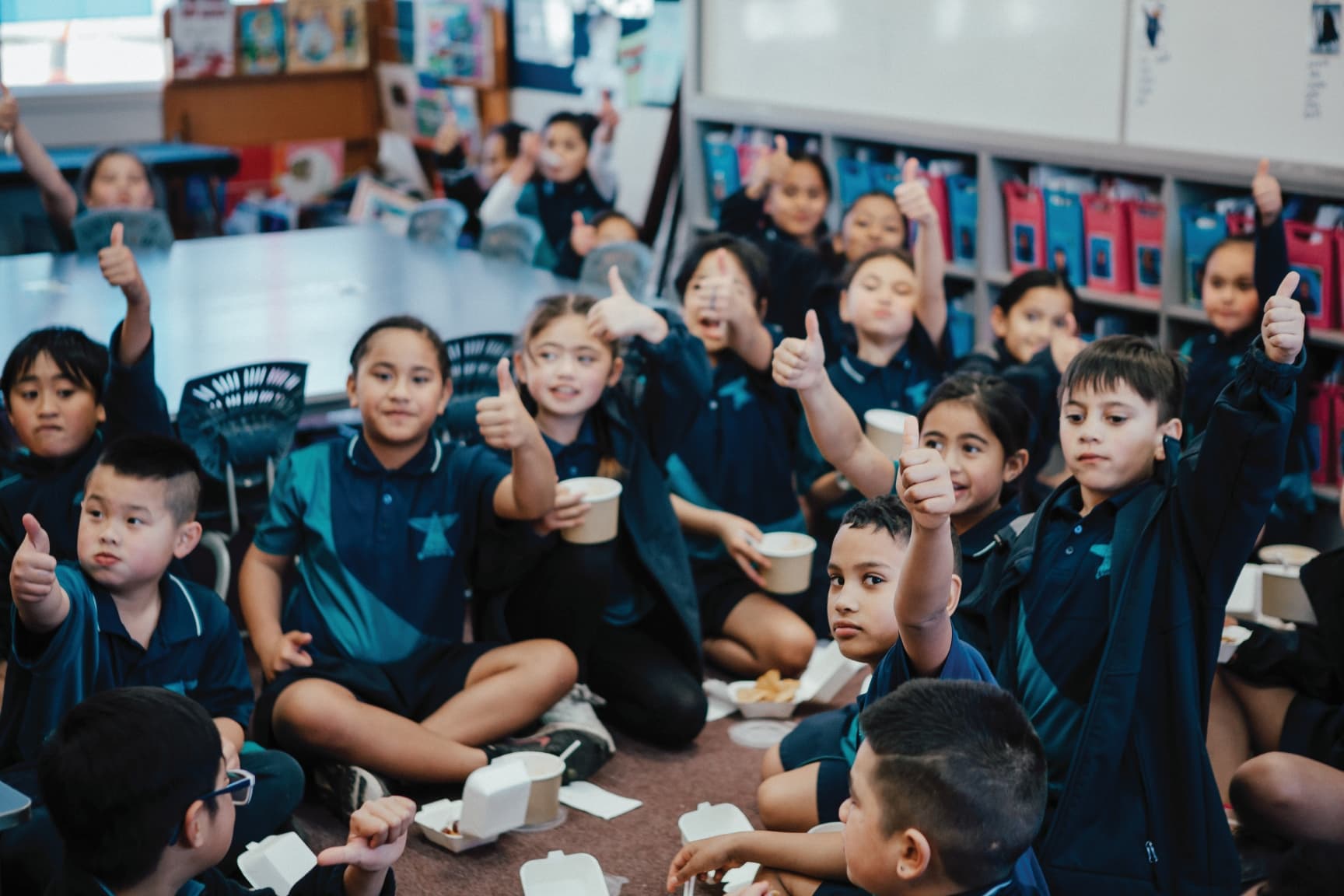 Group of kids sitting on the floor with their Healthy Lunches holding thumbs up