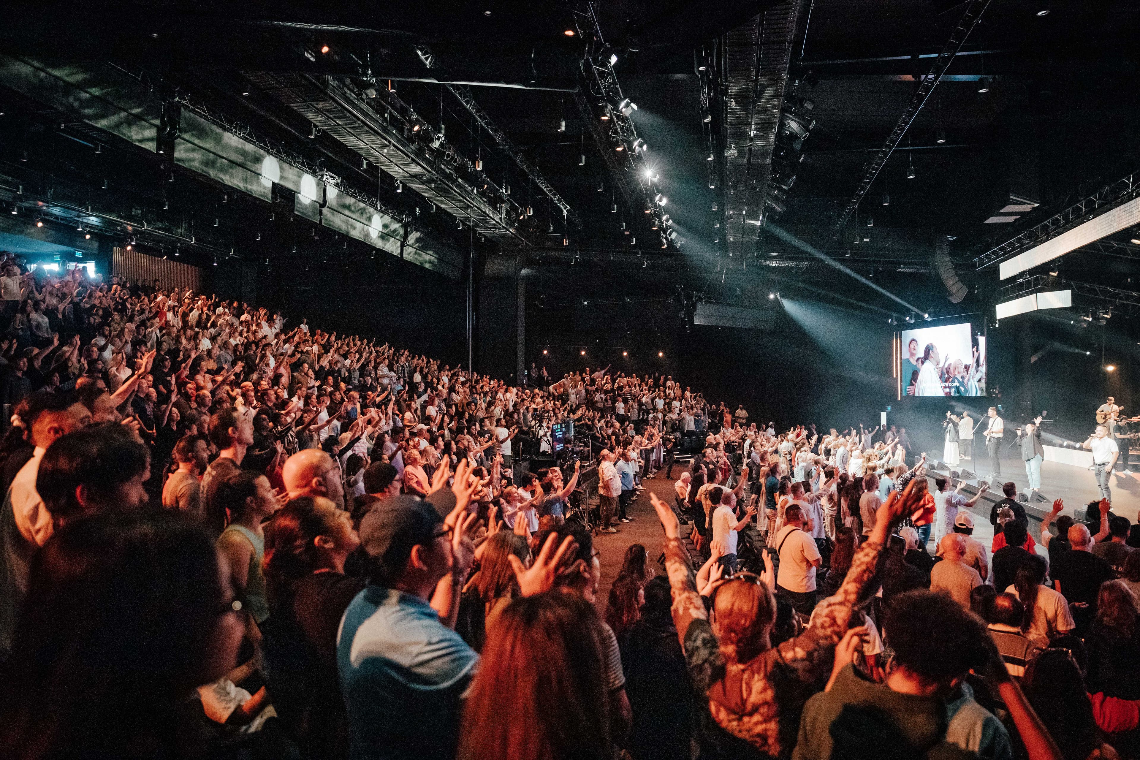 Looking sideways across the Central Campus auditorium at the congregation, many with hands raised in worship