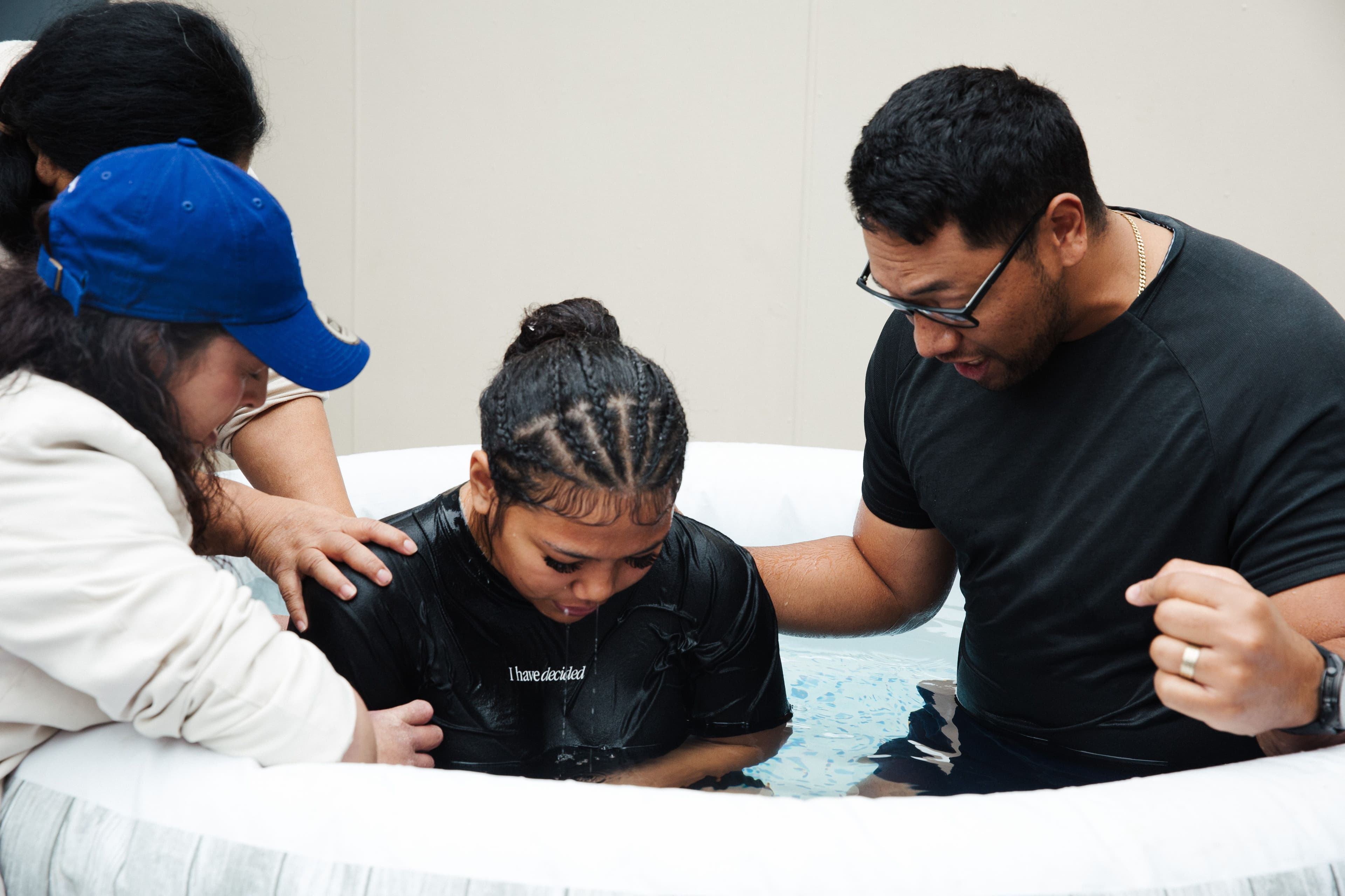 Girl just after being baptised in a small pool with pastors and family laying hands on her shoulders and praying for her