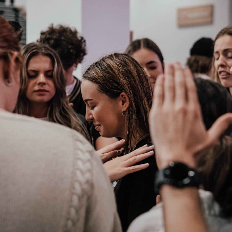 Woman being prayed for surrounded by people praying and laying hands