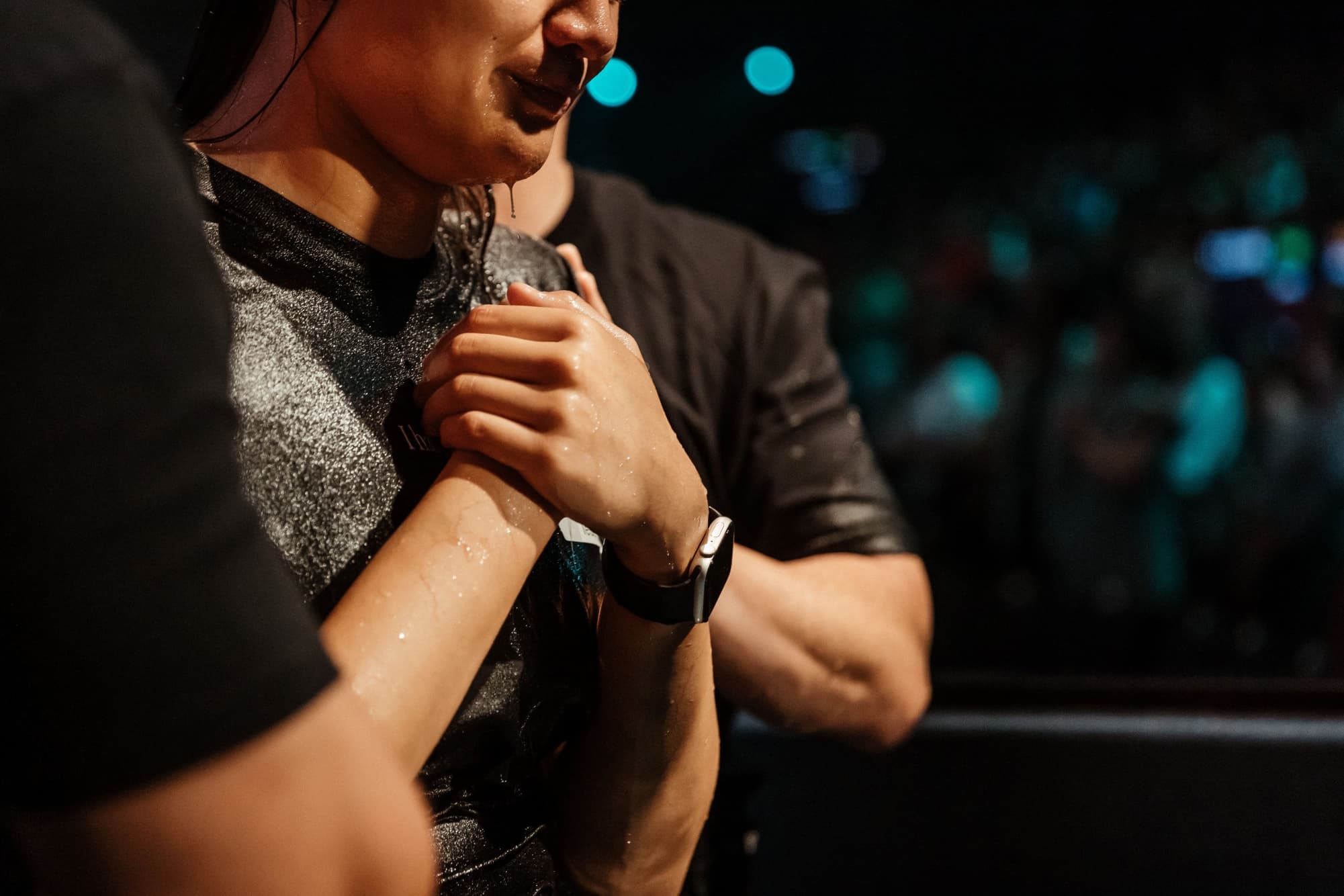 Close up of the side profile of a woman with her hands crossed on her chest with two men either side her praying after she has been baptised