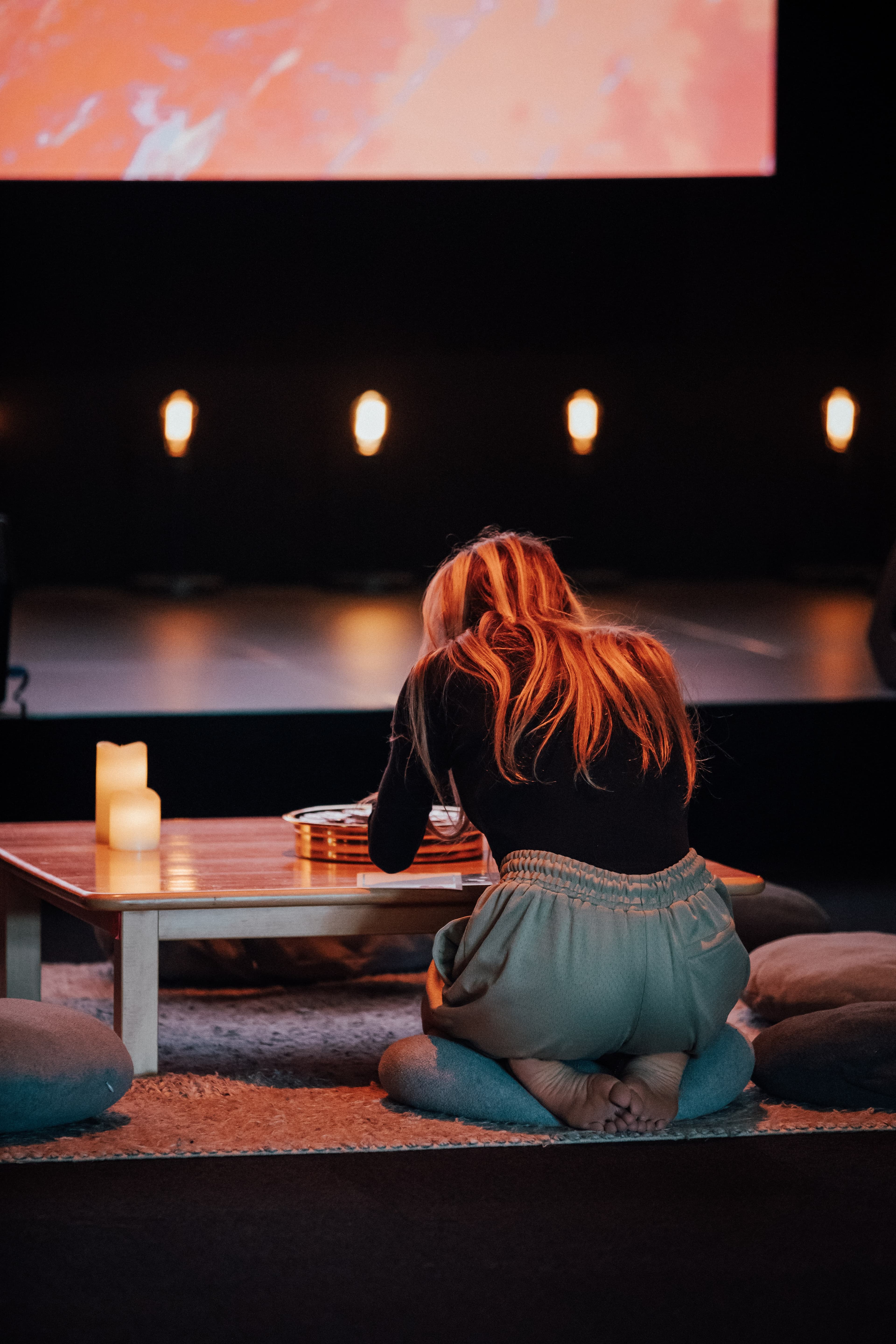 Woman from behind kneeling at a low table with candles and communion set up
